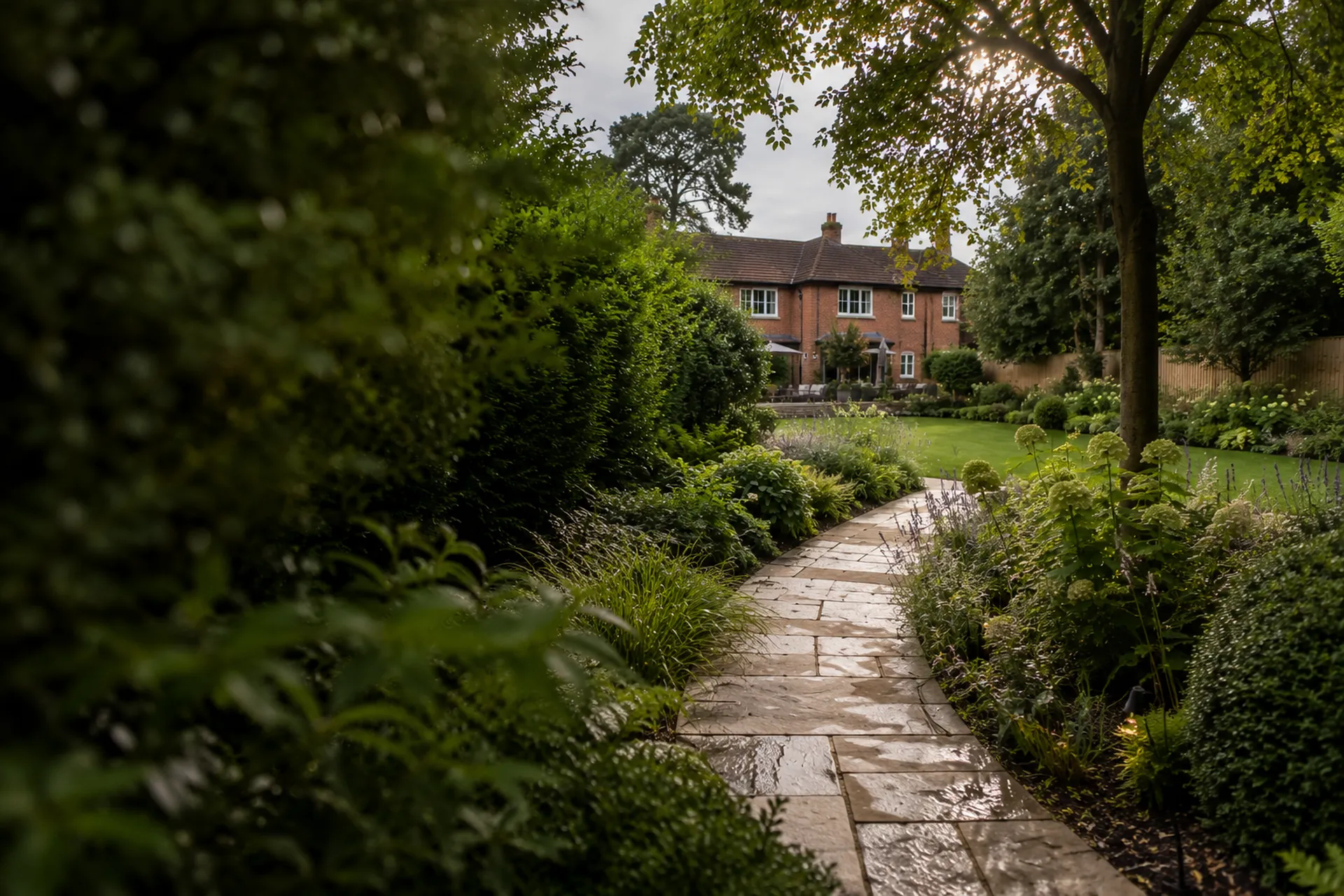 A stone path through layered planting leading to a brick house in a Surrey garden