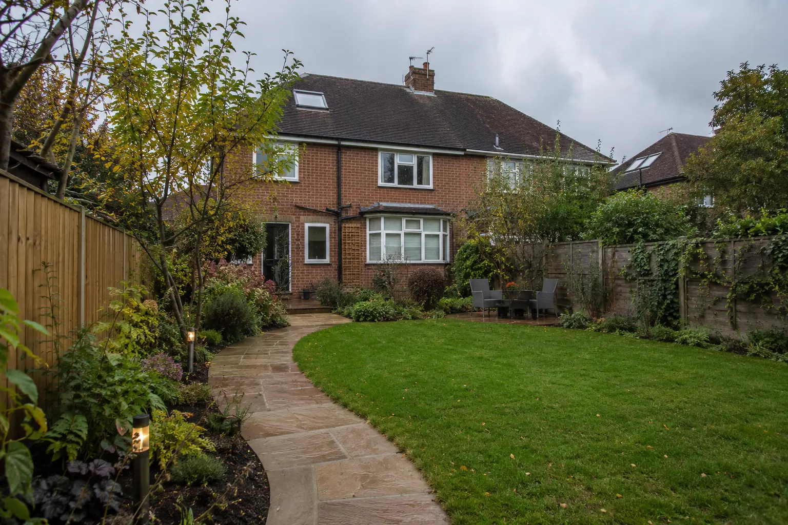 A curved sandstone path through layered planting and a level lawn in a Surrey garden