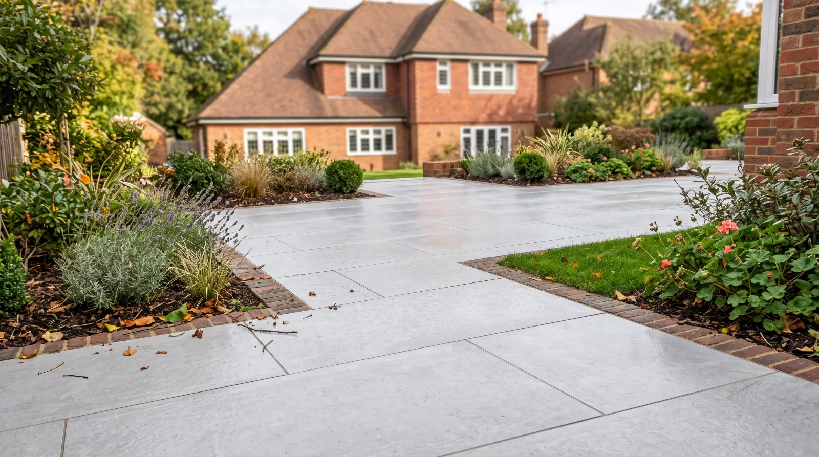 A pristine, light grey porcelain patio with a clean surface and crisp joints, surrounded by neat planting borders and a traditional residential brick home.