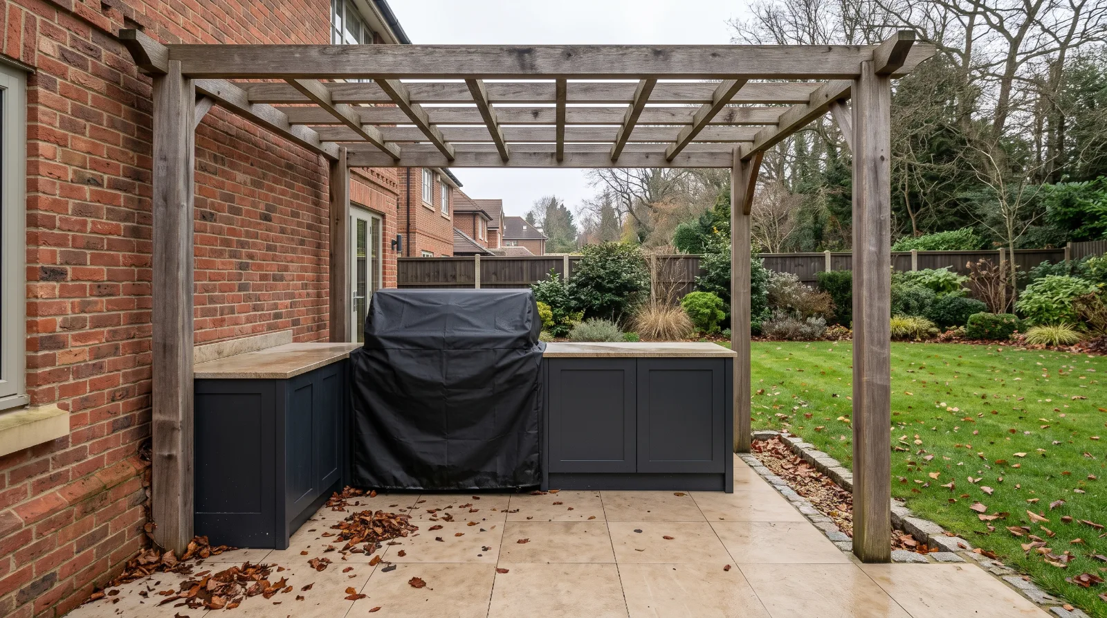 Outdoor kitchen with a protective barbecue cover in a landscaped garden before winter.