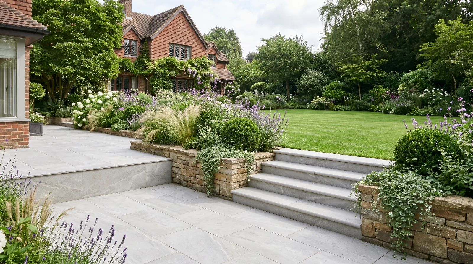 Raised paved patio with retaining wall and steps connecting to a lower garden terrace in a landscaped Surrey garden.